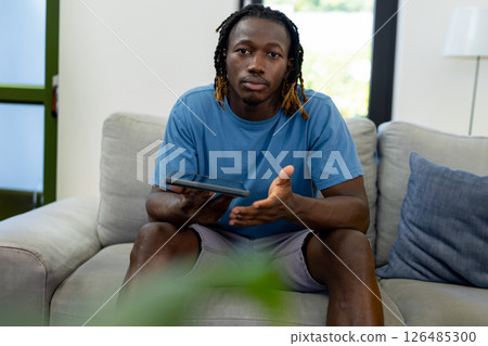 Young man relaxing at home, holding tablet, engaging in casual conversation, copy space Young man relaxing at home, holding tablet, engaging in casual conversation, copy space 126485300