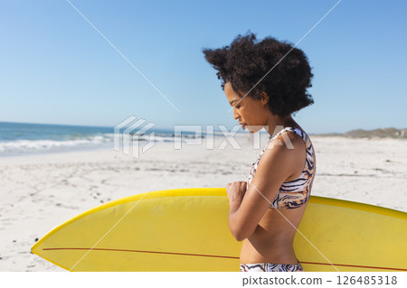 Woman holding surfboard on sunny beach, preparing to surf in vibrant swimwear, copy space 126485318