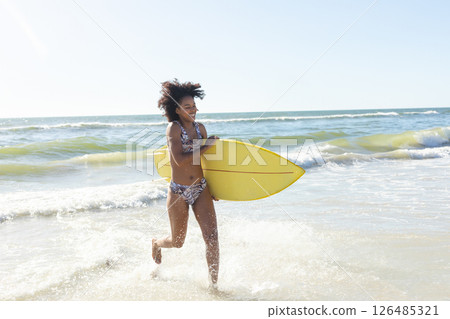 Joyful woman running with surfboard in ocean waves, enjoying sunny beach day, copy space Joyful woman running with surfboard in ocean waves, enjoying sunny beach day, copy space 126485321