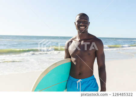 Smiling man holding surfboard on sunny beach, enjoying summer day, copy space 126485322