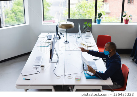 Professional man in mask reviewing documents at modern office desk, copy space 126485328