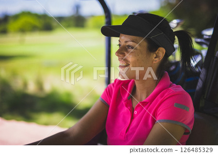 Smiling woman in pink polo shirt enjoying golf cart ride on sunny day, copy space 126485329