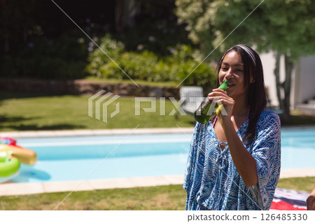 Young woman enjoying cold drink by pool, smiling and relaxing at outdoor party, copy space 126485330