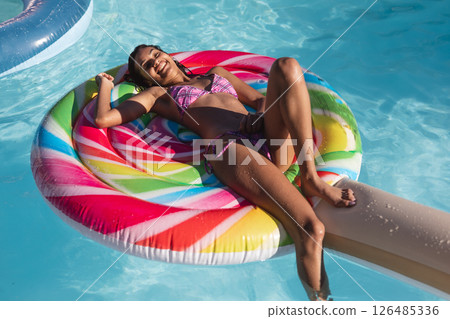Smiling woman relaxing on colorful pool float, enjoying sunny day at pool party, copy space 126485336