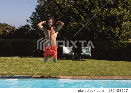 Man jumping into pool wearing orange shorts, enjoying summer fun outdoors, copy space Man jumping into pool wearing orange shorts, enjoying summer fun outdoors, copy space 126485337