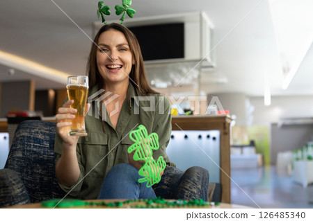 Woman celebrating with beer and shamrock accessories, smiling joyfully at bar, copy space Woman celebrating with beer and shamrock accessories, smiling joyfully at bar, copy space 126485340