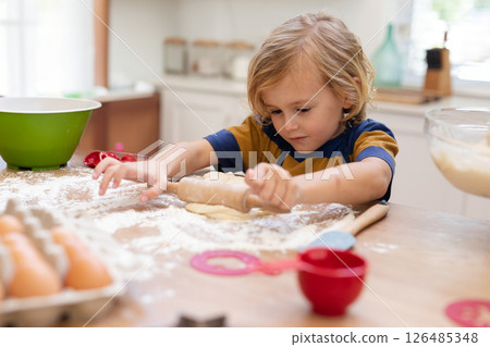 Young boy rolling dough on kitchen counter, enjoying baking at home, copy space 126485348