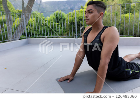 Young man practicing yoga on rooftop terrace, focusing on stretching and relaxation, copy space 126485360