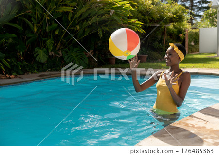 Woman in yellow swimsuit enjoying summer day playing with beach ball in pool, copy space Woman in yellow swimsuit enjoying summer day playing with beach ball in pool, copy space 126485363