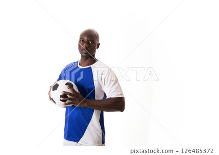 Confident male soccer player holding ball, wearing blue and white jersey, copy space 126485372