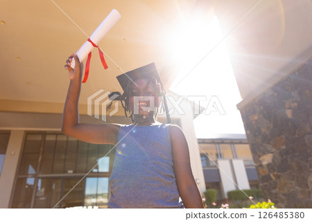 Proud student celebrating graduation outdoors, holding diploma and wearing cap 126485380