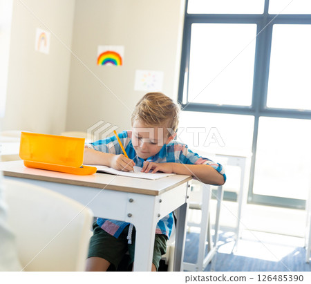 In school, young boy concentrating on writing at desk in bright classroom, copy space In school, young boy concentrating on writing at desk in bright classroom, copy space 126485390