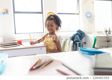 Smiling girl in school writing at desk, enjoying classroom activities, copy space 126485393