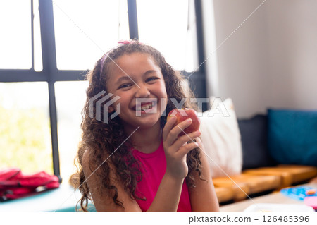 Smiling girl holding apple in school, enjoying healthy snack during break Smiling girl holding apple in school, enjoying healthy snack during break 126485396