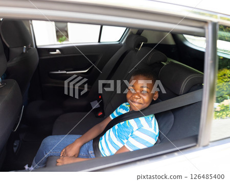 Smiling boy sitting in car backseat, wearing seatbelt, enjoying ride, copy space 126485400