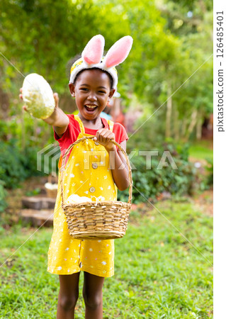 Child in garden wearing bunny ears holding egg and basket, celebrating Easter 126485401