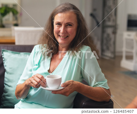 Smiling woman enjoying coffee at home, relaxing on comfortable sofa Smiling woman enjoying coffee at home, relaxing on comfortable sofa 126485407