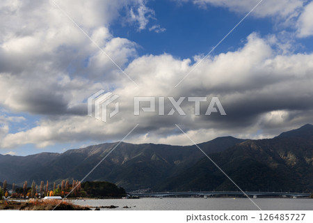 Lake Kawaguchi under a vast cloudy sky with autumn trees and mountains surrounding the water Lake Kawaguchi under a vast cloudy sky with autumn trees and mountains surrounding the water 126485727