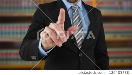 Businessman in suit pointing at camera in office with bookshelves behind 126485788