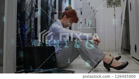Stressed woman sitting on server room floor with laptop, facing technical issues 126485800