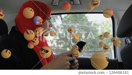 Woman in red hijab using smartphone in car surrounded by floating emojis 126486181