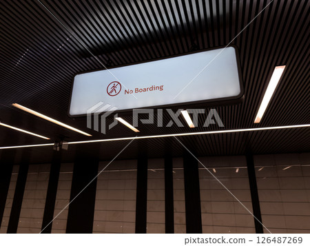 Well lit modern metro station interior with large illuminated No Boarding sign hanging from the ceiling, emphasizing rules and structure in urban public transportation spaces 126487269