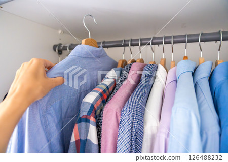 Male hand selecting a shirt from a wardrobe full of clothes on wooden hangers. Concept of clothing choice, daily routine and personal style. 126488232