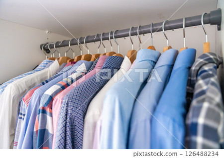Neatly arranged men shirts hanging on wooden hangers in wardrobe. Minimalist clothing organization and classic male fashion concept Neatly arranged men shirts hanging on wooden hangers in wardrobe. Minimalist clothing organization and classic male fashion concept 126488234