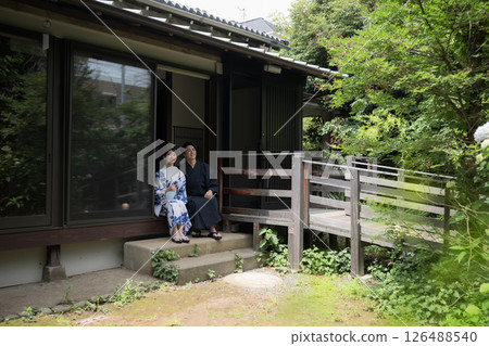 Image of a couple or married couple on a hot spring trip or sightseeing in yukata, sitting on the veranda and gazing at the viewer, wide-angle 126488540