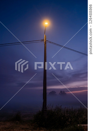 A Mysterious Fog at Dusk Surrounds a Glowing Streetlamp in the Evening Atmosphere A Mysterious Fog at Dusk Surrounds a Glowing Streetlamp in the Evening Atmosphere 126488866