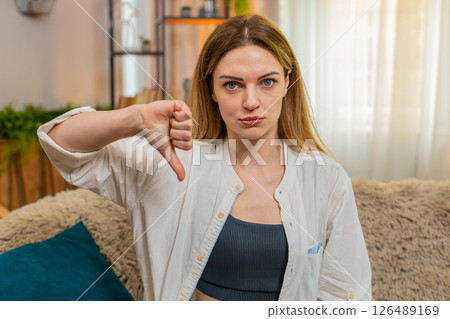 Adult sad woman showing thumbs down at home, looking serious, expressing disagreement disapproval Adult sad woman showing thumbs down at home, looking serious, expressing disagreement disapproval 126489169