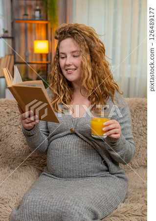 Pregnant young woman drinking orange juice while reading pregnancy book at home, calm relaxed mood Pregnant young woman drinking orange juice while reading pregnancy book at home, calm relaxed mood 126489177