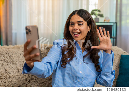 Indian woman recording story on smartphone at home, talking with hand gestures sitting on sofa 126489183