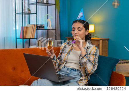 Celebrating Indian woman holding champagne glass enjoying birthday talking online video call joyful Celebrating Indian woman holding champagne glass enjoying birthday talking online video call joyful 126489224