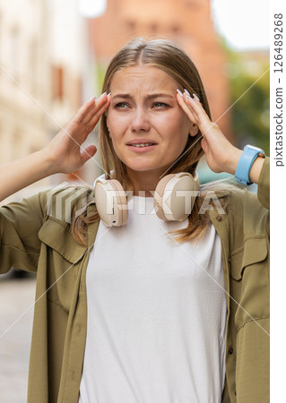 Displeased exhausted young Caucasian woman girl rubbing temples to cure headache on city street 126489268