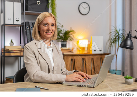 Happy mature businesswoman in formal suit with laptop after finishing work at desk in home office 126489299