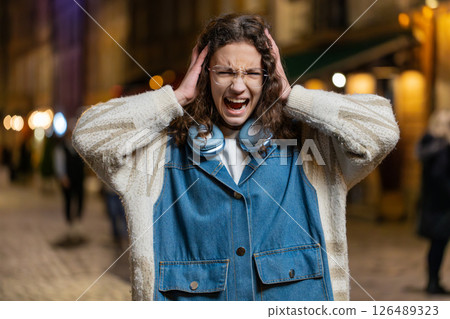 Displeased angry girl frowns face feels disgust suffering from loud sound covers ears with hands 126489323