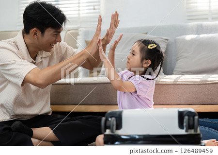 Playful Interaction and Family Engagement. A father and daughter sharing a playful moment with a suitcase. 126489459