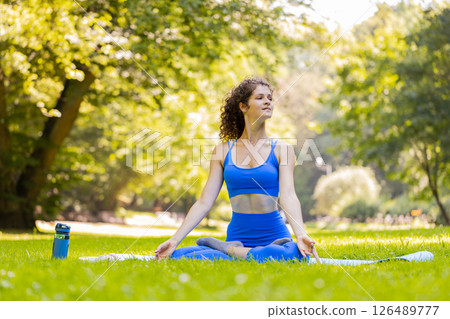 Woman sitting on mat in lotus position, relaxing practicing yoga meditation in park on summer day Woman sitting on mat in lotus position, relaxing practicing yoga meditation in park on summer day 126489777
