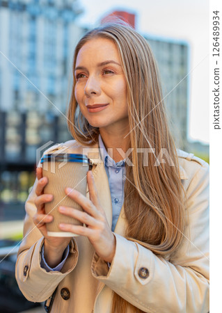 Happy mature businesswoman enjoying morning coffee hot drink and smiling on downtown city street Happy mature businesswoman enjoying morning coffee hot drink and smiling on downtown city street 126489934
