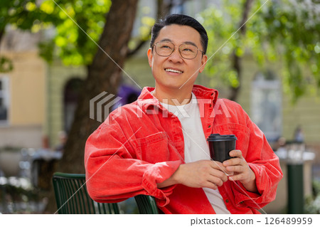 Happy Asian man enjoying drinking morning coffee hot drink, relaxing, taking a break on city street Happy Asian man enjoying drinking morning coffee hot drink, relaxing, taking a break on city street 126489959