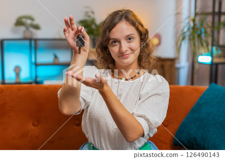 Happy young woman real estate agent sitting on sofa showing the keys of new home house apartment 126490143