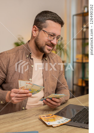 Rich happy Caucasian man counting money euro cash using laptop calculate domestic bills at home 126490162