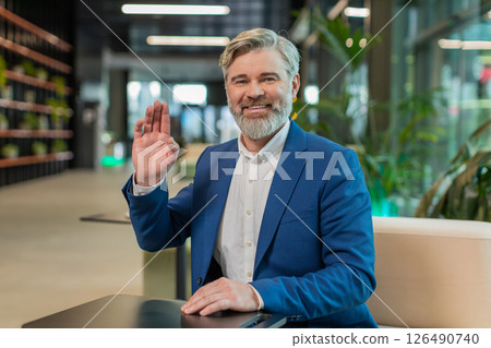Happy middle-aged Caucasian businessman looking at camera and waving hand hello in office lobby 126490740
