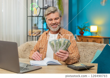 Mature man sitting on sofa table with laptop and calculator, managing family budget at home Mature man sitting on sofa table with laptop and calculator, managing family budget at home 126490783