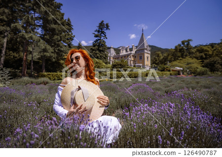 A woman wearing a straw hat sits in a field of purple flowers 126490787