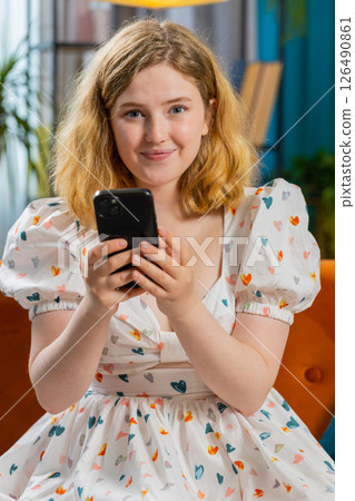 Young woman sitting on sofa at home, using smartphone share messages on social media application 126490861