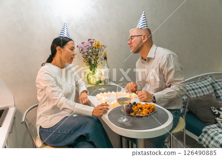 Couple Birthday Celebration Home: Romantic indoor birthday celebration, a couple blows out candles on a cake at home, intimate moment. Couple Birthday Celebration Home: Romantic indoor birthday celebration, a couple blows out candles on a cake at home, intimate moment. 126490885