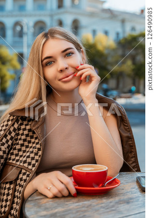 Woman Coffee Cafe Outdoor Relaxing - Blonde woman smiles, holding red cup of coffee, while sitting at a table outside a cafe. 126490985