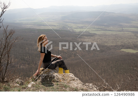 Woman Landscape Relaxation: Lady rests on rock outcrop above scenic valley landscape, sunny day for enjoying view. Woman Landscape Relaxation: Lady rests on rock outcrop above scenic valley landscape, sunny day for enjoying view. 126490986